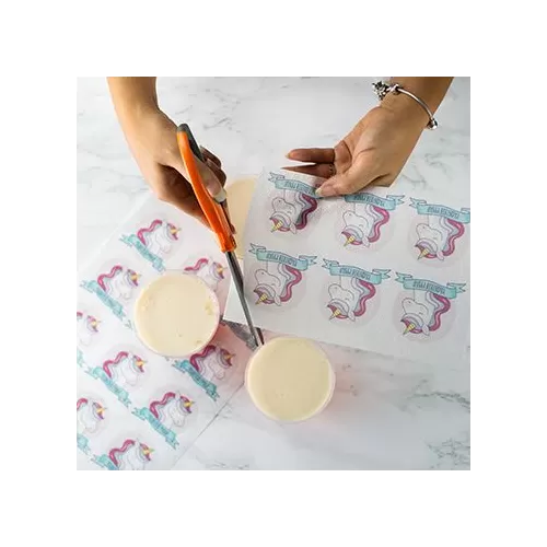 Hands using scissors to cut edible cake toppers featuring unicorn designs on a flat surface.