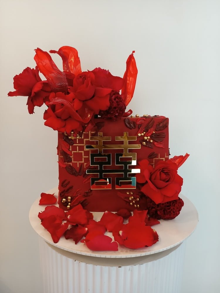 A red cake adorned with flowers and decorative elements, featuring a gold symbol.