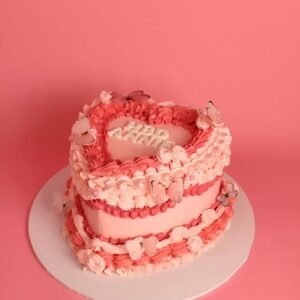 Heart-shaped cake with pink buttercream frosting and decorative butterflies on a white cake board. vintage cake, retro cake, birthday cake, pink cake
