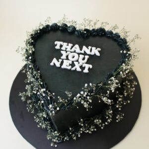 Heart-shaped cake with black frosting and white text saying 'Thank You Next' surrounded by decorative flowers. vintage cake, breakup cake, seperation cake, divorce cake