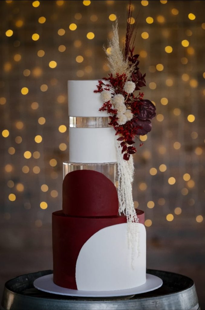 Three-tier wedding cake featuring white and burgundy layers with floral accents.