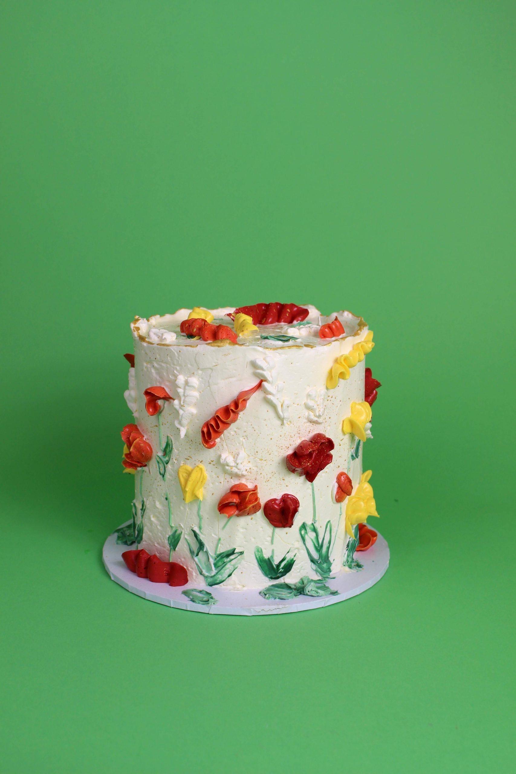 A round cake decorated with colorful floral designs made of icing on a green background. floral cake, floral piping, birthday cake, celebration cake