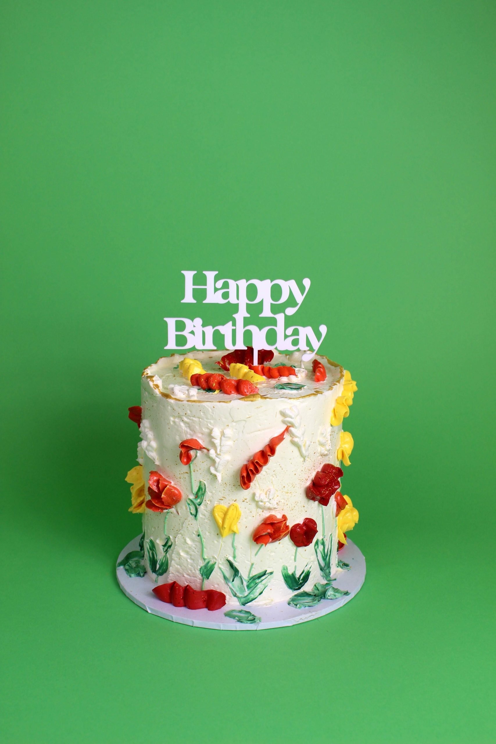 A birthday cake decorated with flowers and a 'Happy Birthday' sign on a green background. floral cake, floral piping, birthday cake, celebration cake