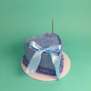 Heart-shaped purple cake decorated with a blue ribbon and a candle on top. bow cake, vintage cake, birthday cake