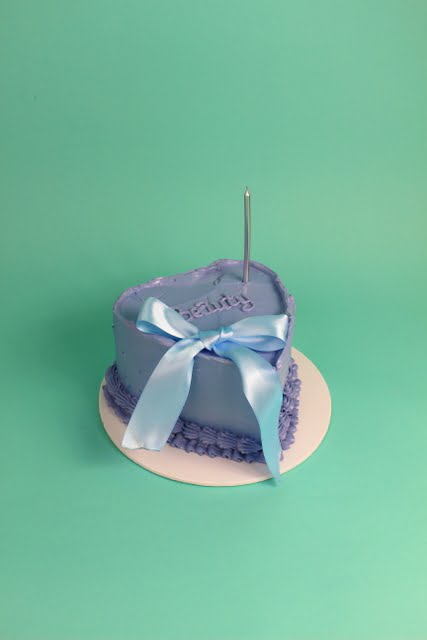 Heart-shaped purple cake decorated with a blue ribbon and a candle on top. bow cake, vintage cake, birthday cake