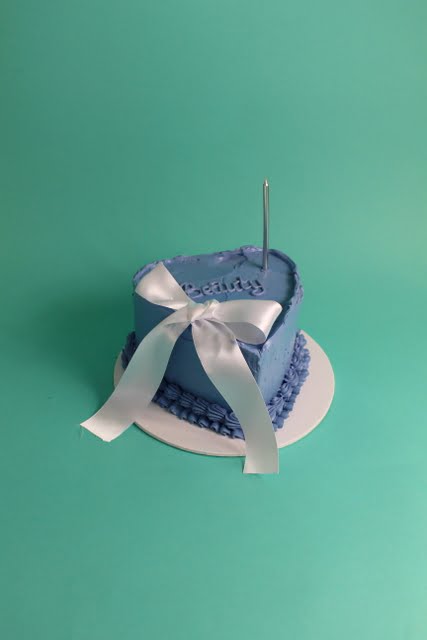 A blue heart-shaped cake decorated with a white ribbon and a single candle on top. bow cake, vintage cake, birthday cake