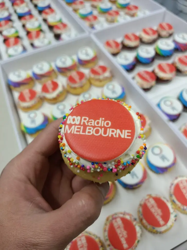 Cupcake topped with a red circle featuring the Radio Melbourne logo and colorful sprinkles. ABC radio melbourne,corporate cupcakes, business launch