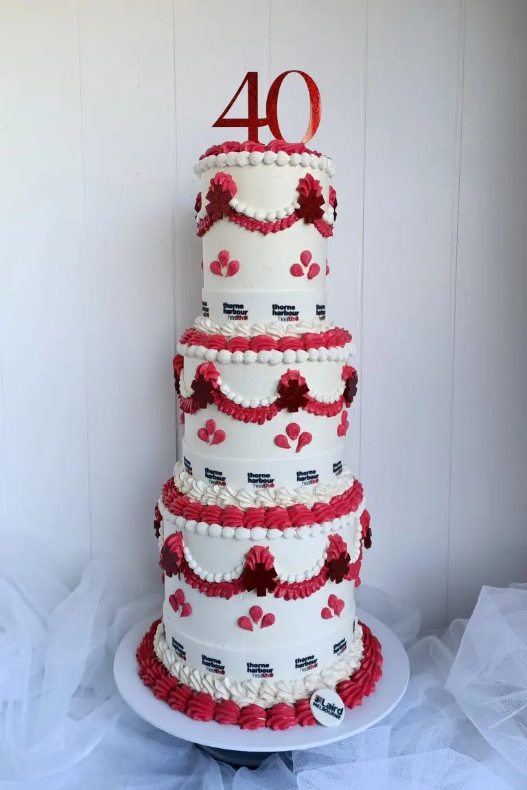 Four-tiered white cake decorated with red and pink accents and a '40' topper. corporate cake, business launch, company cake