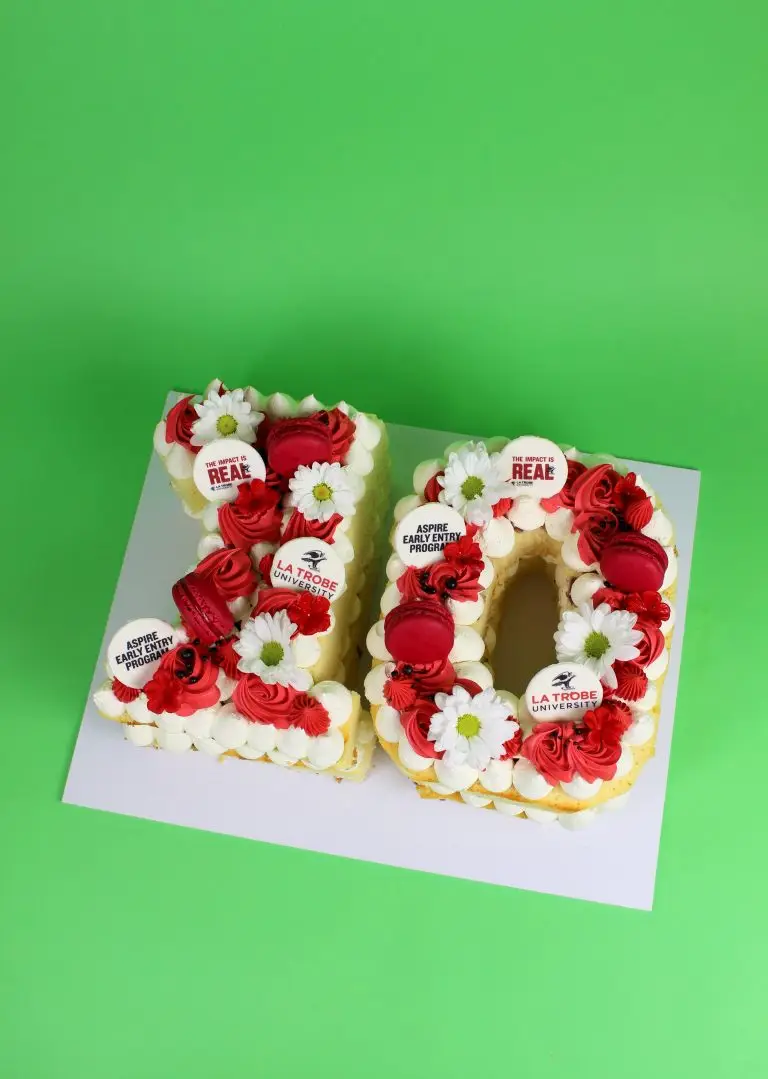 Cake shaped as the number 12, decorated with red roses and white flowers on a green background. corporate cake, business launch, company cake, number cake