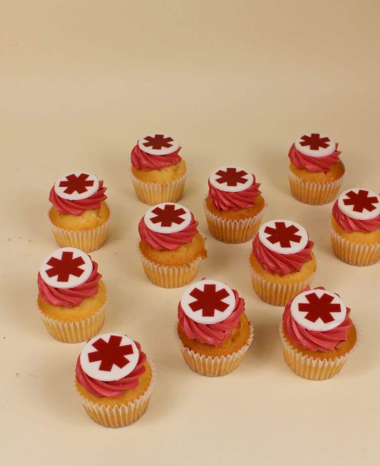 Cupcakes topped with red frosting and white decorations featuring a red cross symbol. corporate cupcake, business launch, company cake,