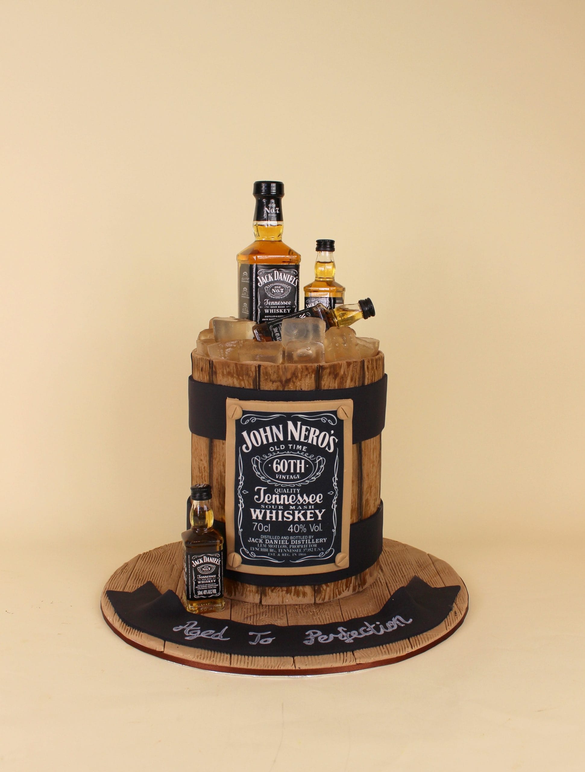 A cake designed to resemble a whiskey barrel with miniature whiskey bottles on top. whiskey cake, adult birthday cake, 60th birthday cake, male birthday cake